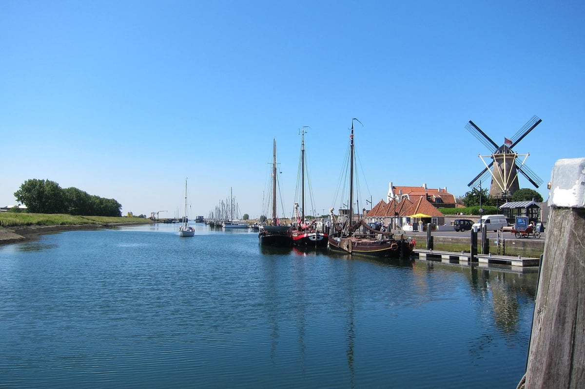 Zeilboten in de haven met een traditionele molen en groen landschap onder een blauwe lucht