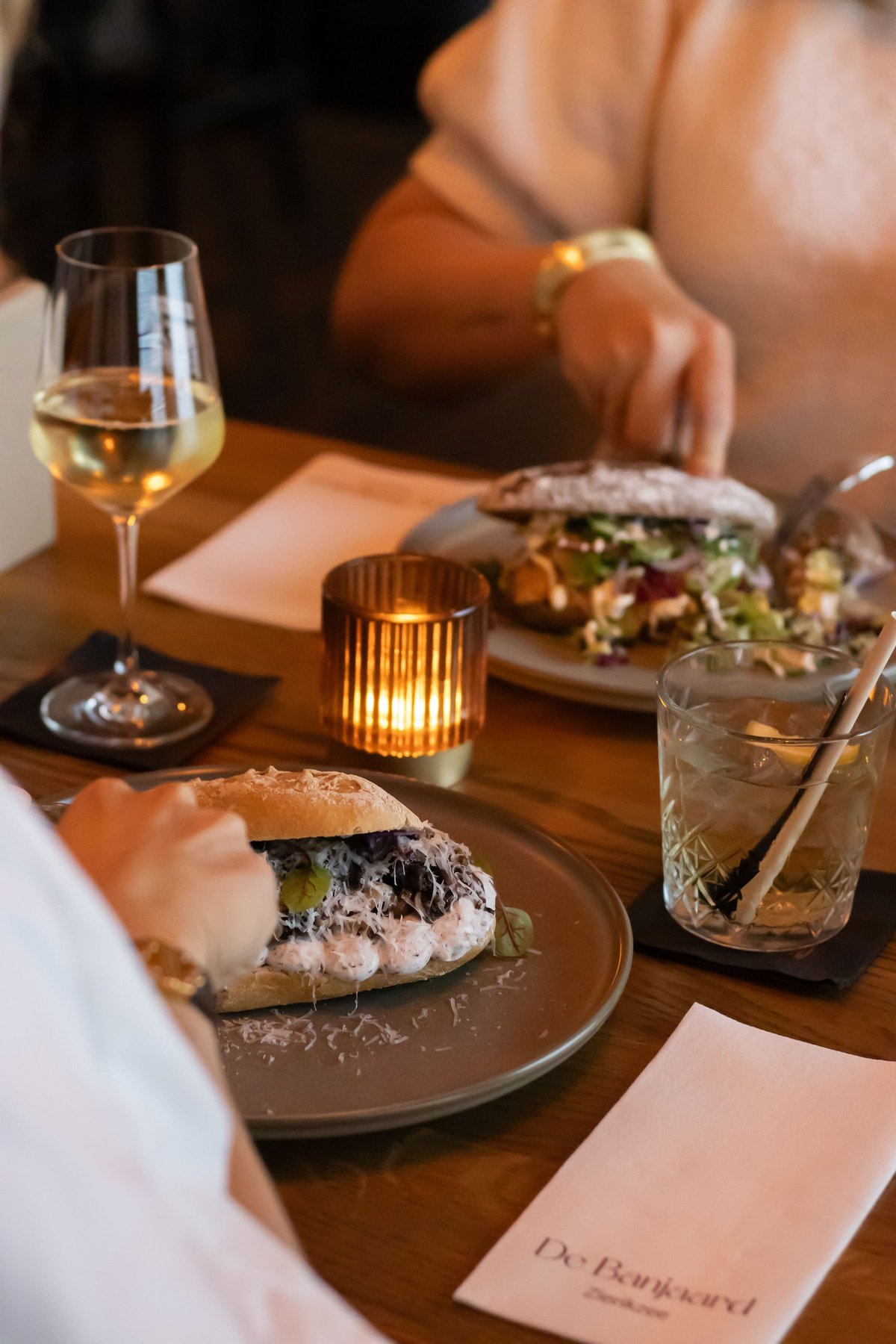 Gedekte tafel bij De Banjaard met broodjes, een glas witte wijn, een cocktail en kaarslicht